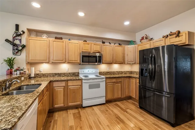 a kitchen with stainless steel appliances granite countertop a refrigerator a sink dishwasher a stove and white countertops with wooden floor