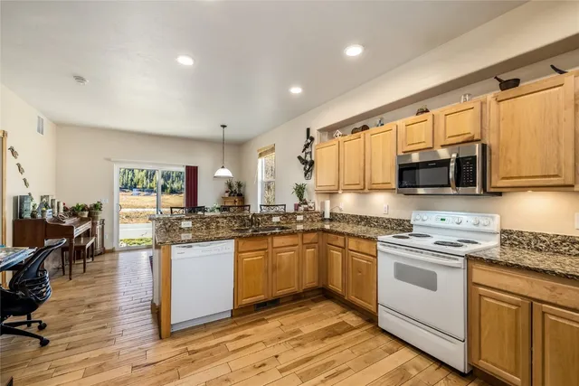 a kitchen with stainless steel appliances granite countertop a stove top oven a sink dishwasher a refrigerator and a dining table with wooden floor