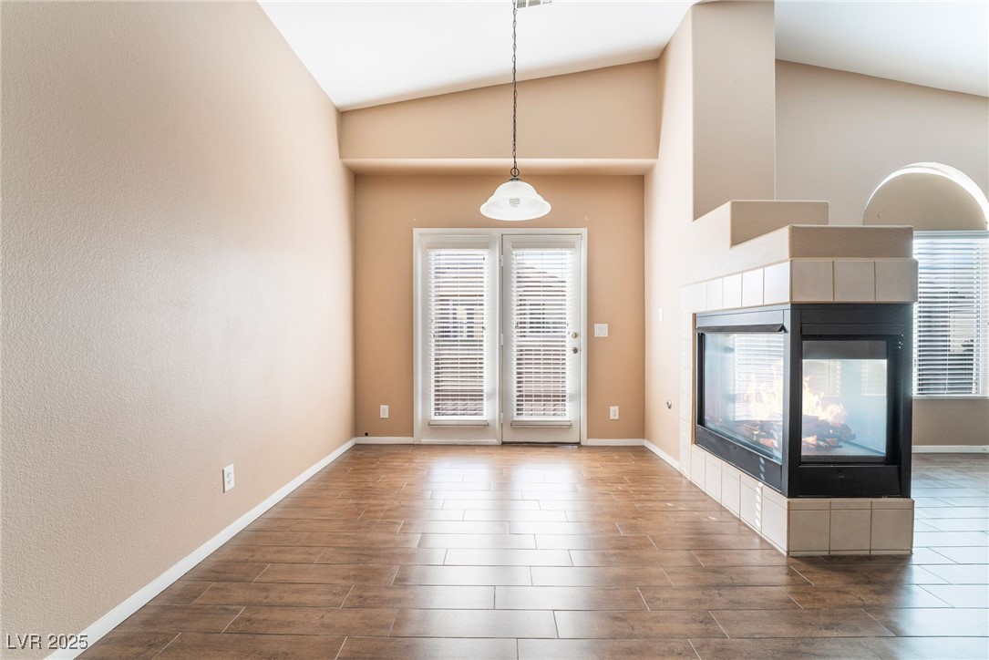1570 Rusty Ridge Lane Henderson, NV 89002 - Photo 9 of 35 Unfurnished living room featuring dark wood-style flooring, baseboards, high vaulted ceiling, and a tiled fireplace
