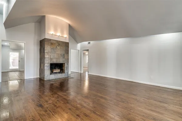 a view of an empty room with wooden floor fireplace and a window