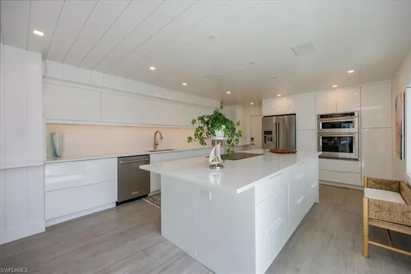 a large white kitchen with a sink and dishwasher a stove top oven with wooden floor