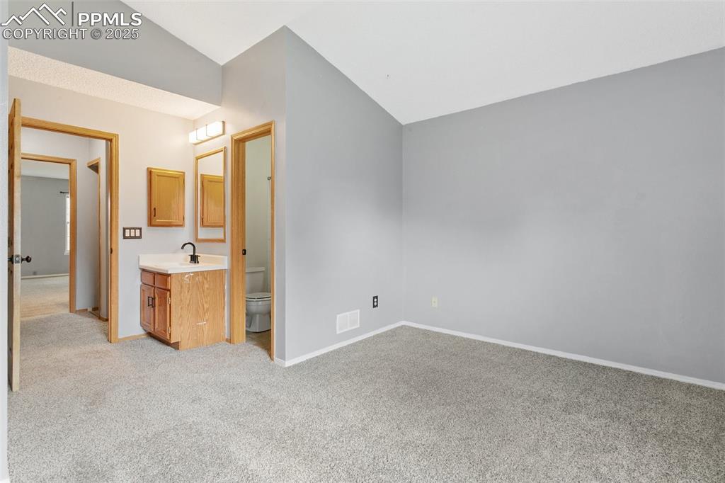 3457 Queen Anne Way Colorado Springs, CO 80917 - Photo 17 of 25 Unfurnished bedroom featuring vaulted ceiling, light carpet, and connected bathroom