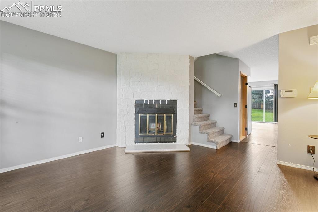 3457 Queen Anne Way Colorado Springs, CO 80917 - Photo 4 of 25 Unfurnished living room with wood finished floors, a stone fireplace, and stairway