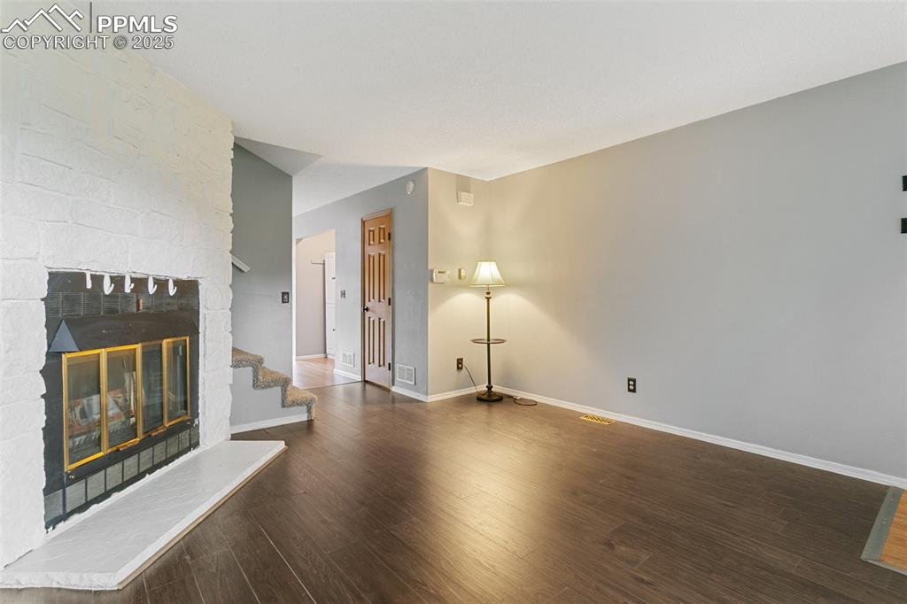 3457 Queen Anne Way Colorado Springs, CO 80917 - Photo 5 of 25 Unfurnished living room with wood finished floors, stairs, and a stone fireplace