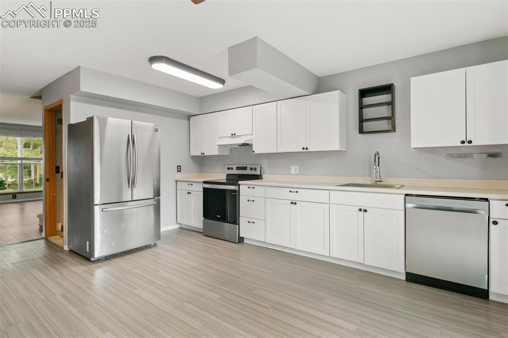 3457 Queen Anne Way Colorado Springs, CO 80917 - Photo 7 of 25 Kitchen featuring stainless steel appliances, under cabinet range hood, light countertops, light wood-style flooring, and white cabinetry