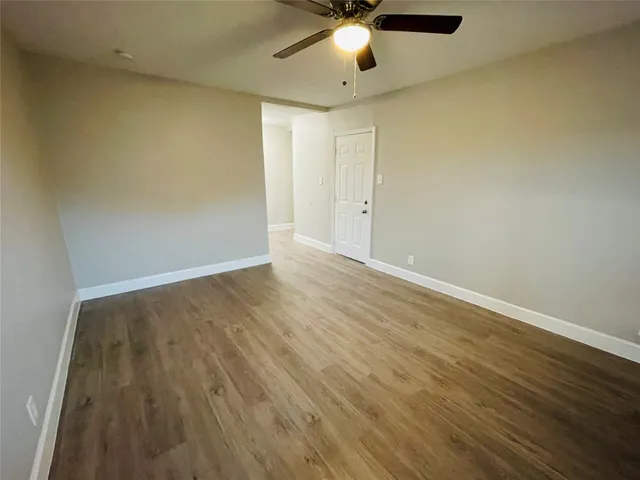 an empty room with wooden floor chandelier fan and windows