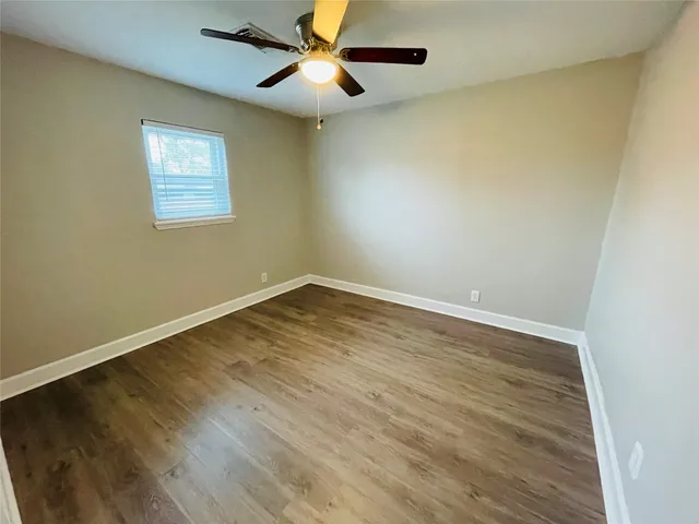 a view of an empty room with wooden floor and a ceiling fan
