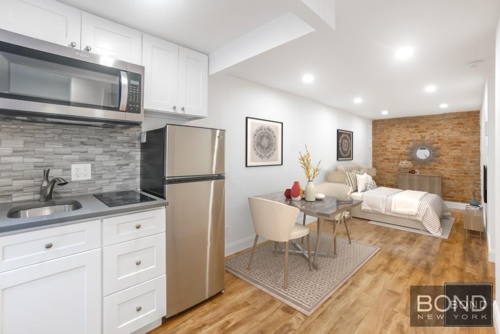 a living room with stainless steel appliances kitchen island granite countertop a refrigerator a stove a sink dishwasher and white cabinets with wooden floor