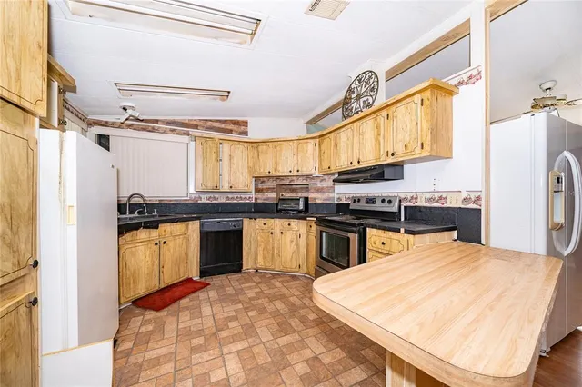 a kitchen with stainless steel appliances kitchen island granite countertop a refrigerator a sink dishwasher a stove and white cabinets with wooden floor