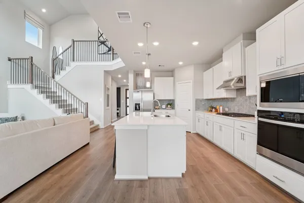 a large white kitchen with kitchen island a stove a sink a center island and wooden floor