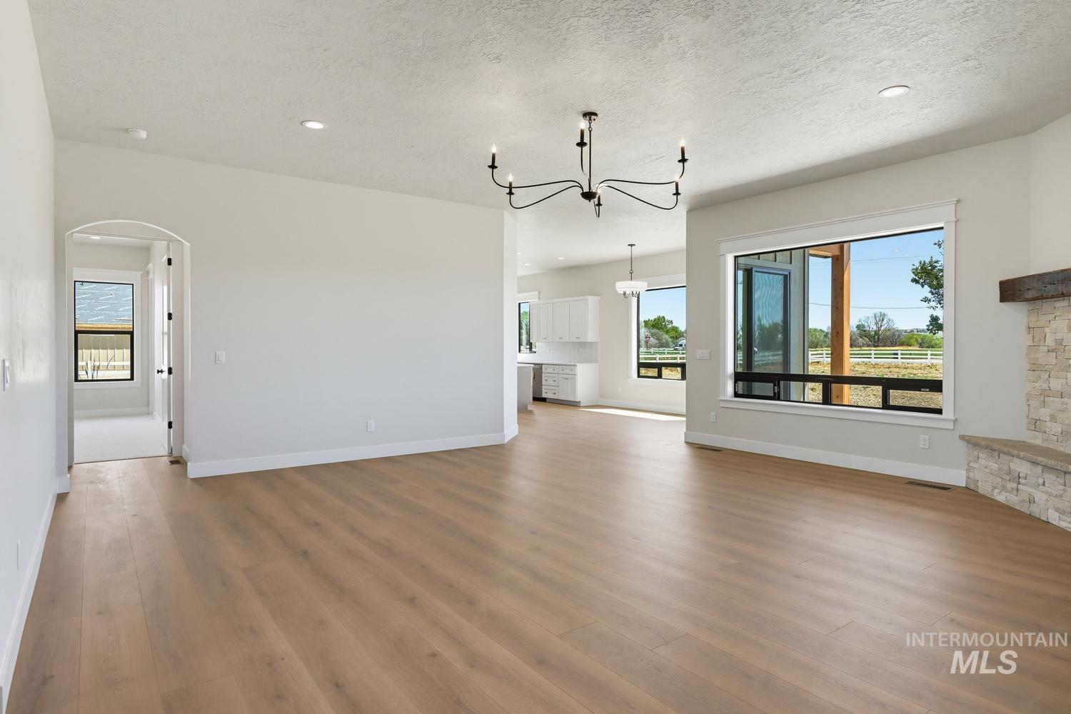5054 Heritage Drive Marsing, ID 83639 - Photo 15 of 38 Open-concept interior featuring wood-finish flooring, a contemporary chandelier, recessed lighting, expansive windows, and a stone-faced fireplace with a rustic wood mantel