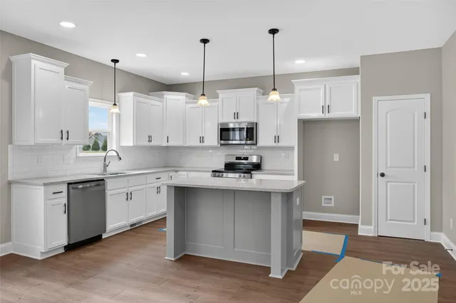 a kitchen with stainless steel appliances granite countertop a sink a stove a refrigerator and white cabinets with wooden floor