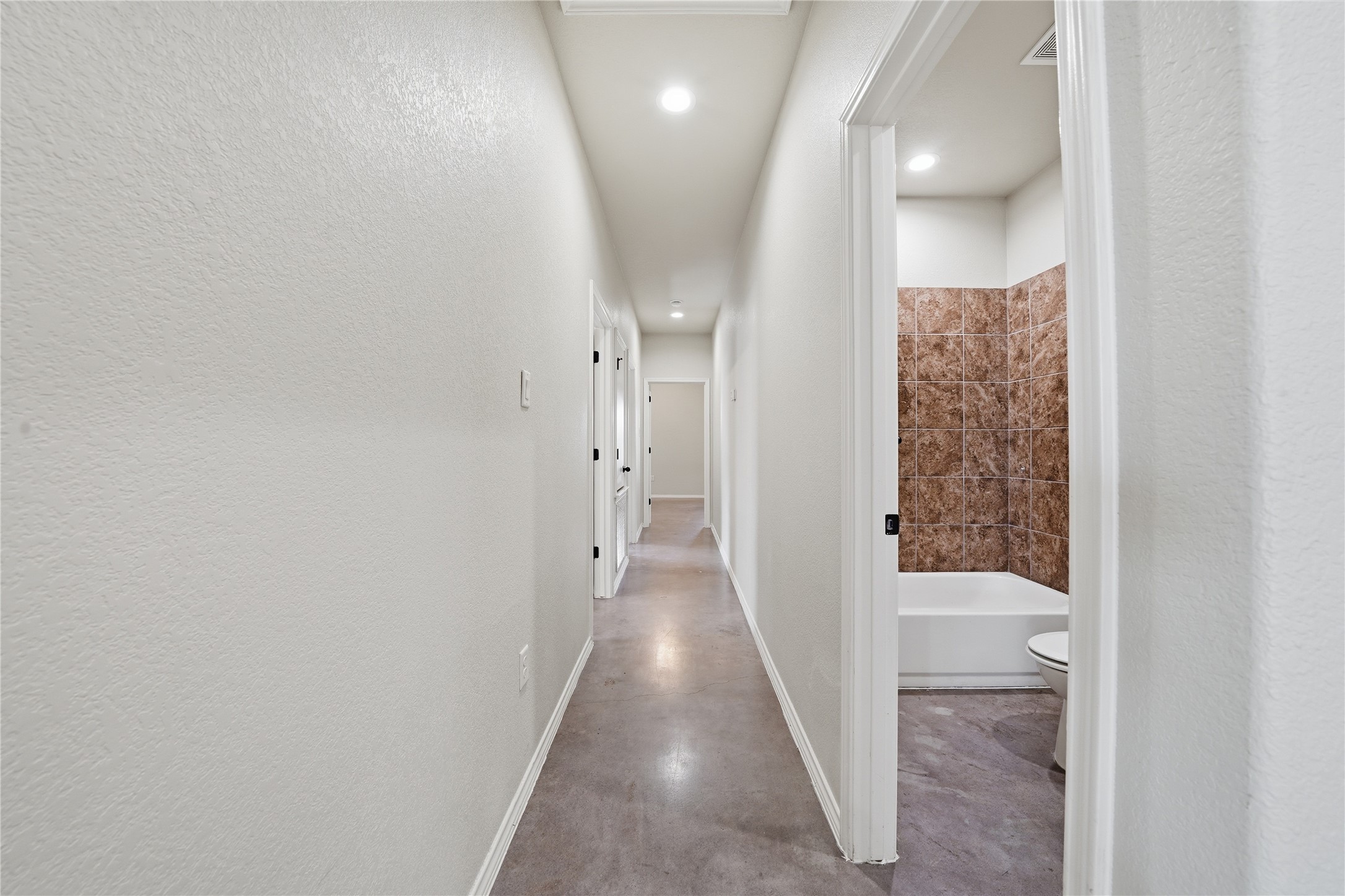 533 Jack Rabbit Lane, Unit A Buda, TX 78610 - Photo 9 of 34 A long, bright hallway features a simple bath with tiled shower surround, offering practical living.