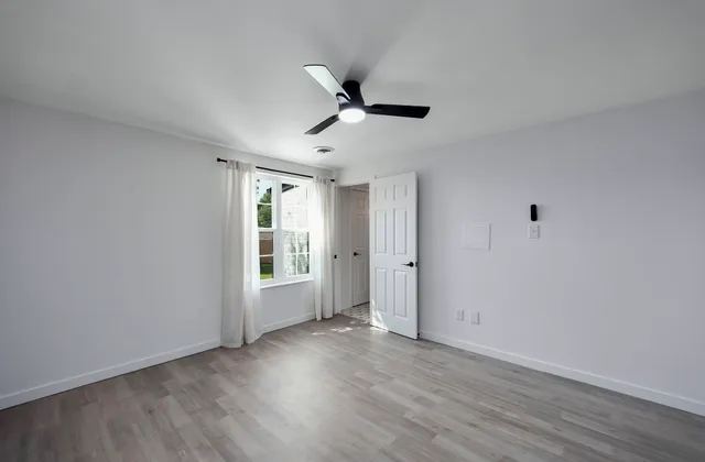 a view of an empty room with wooden floor and a window