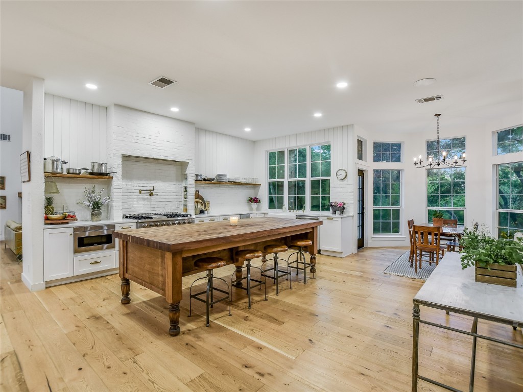 a kitchen with stainless steel appliances granite countertop a stove top oven a sink a dining table and chairs with wooden floor