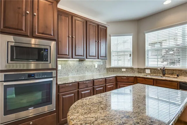 a kitchen with stainless steel appliances kitchen island granite countertop wooden cabinets a stove and a sink