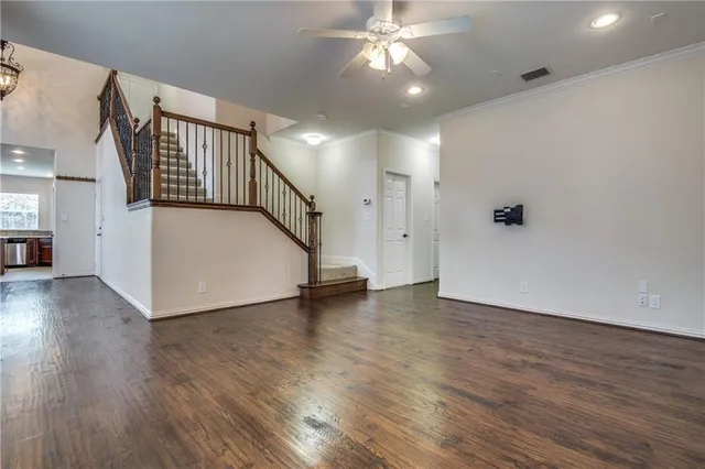a view of an empty room with wooden floor and a ceiling fan