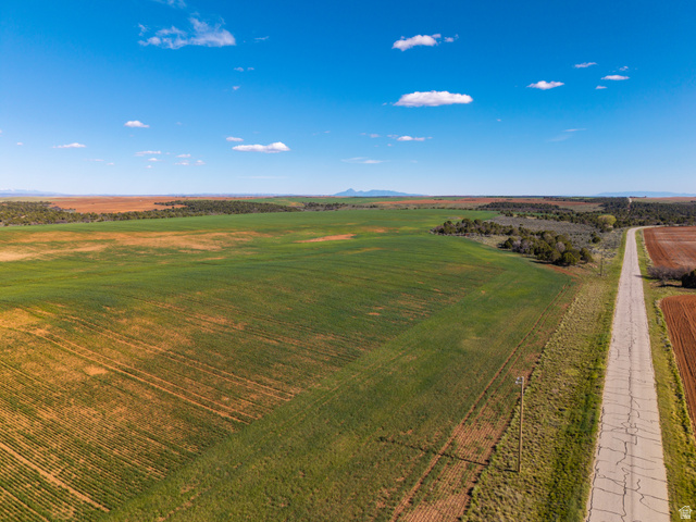 412 South Eastland Road Monticello, UT 84535 - Photo 6 of 14 Expansive agricultural land featuring a paved road bordering cultivated fields, a mix of green crops and reddish-brown soil, and distant mountain ranges under a clear sky
