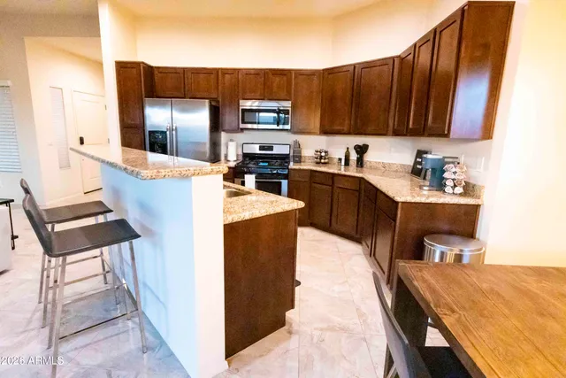 a kitchen with stainless steel appliances kitchen island granite countertop a refrigerator a stove and a sink with wooden cabinets