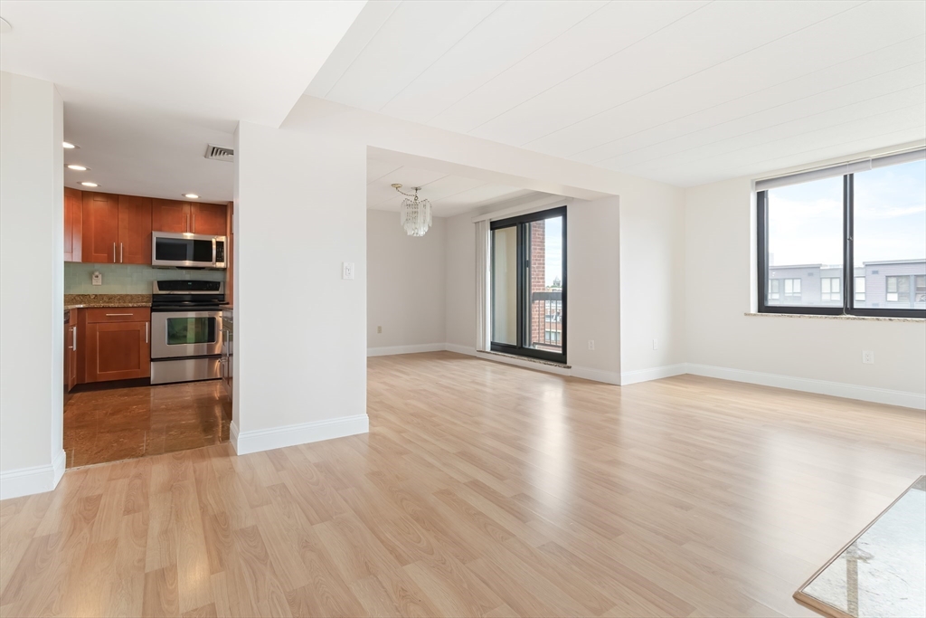 85 Brainerd Road, Unit 507 Boston, MA 02134 - Photo 5 of 23 an empty room with wooden floor kitchen view and windows