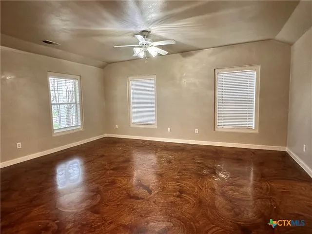 an empty room with wooden floor chandelier fan and windows