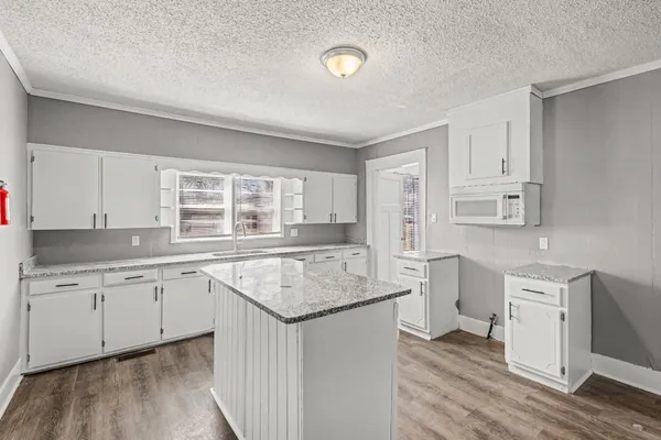 a living room with stainless steel appliances kitchen island granite countertop wooden floor and cabinets
