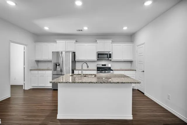 a large kitchen with stainless steel appliances granite countertop a stove a sink a refrigerator white cabinets and chairs with wooden floor