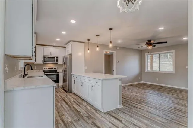 a kitchen with granite countertop a refrigerator oven a sink dishwasher and white cabinets with wooden floor