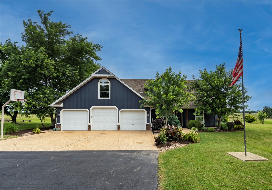 16556 East Hewitt Springs Road Springdale, AR 72764 - Photo 4 of 60 Exterior featuring dark blue siding, a multi-car garage, a dormer window with an arched top, a concrete driveway, and mature landscaping