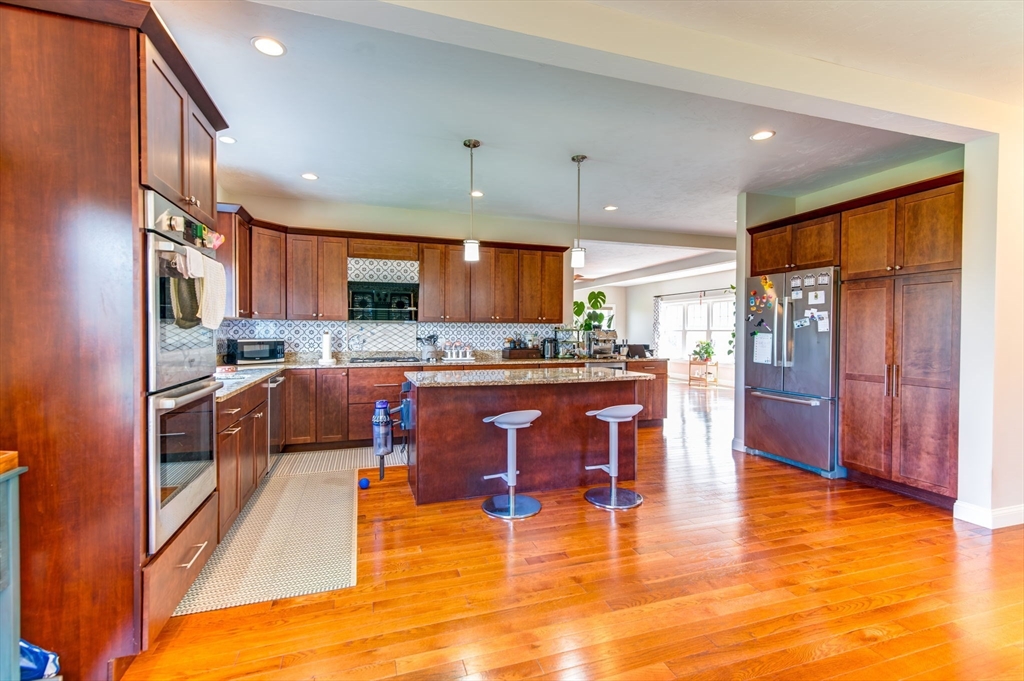 51 Tamarack Road Dracut, MA 01826 - Photo 10 of 39 a kitchen with stainless steel appliances kitchen island granite countertop a refrigerator a stove a sink a dining table and chairs with wooden floor