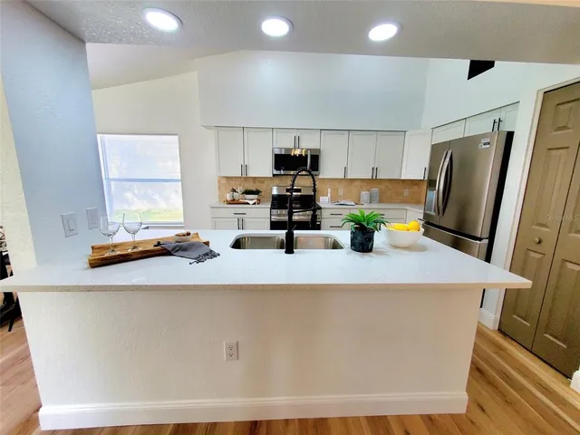 a kitchen with stainless steel appliances a refrigerator a sink a stove a microwave a refrigerator and white cabinets