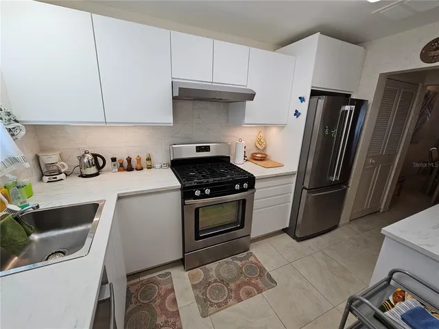 a kitchen with stainless steel appliances a refrigerator a sink a stove and white cabinets