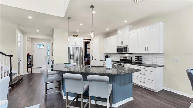 a large kitchen with stainless steel appliances kitchen island granite countertop a dining table chairs and a refrigerator