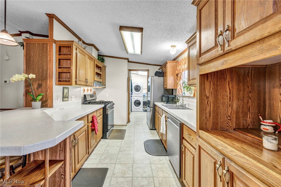 27202 Cook Road, Unit 95 Olmsted Falls, OH 44138 - Photo 15 of 46 Kitchen with open shelves, crown molding, stainless steel appliances, a textured ceiling, and stacked washer / dryer