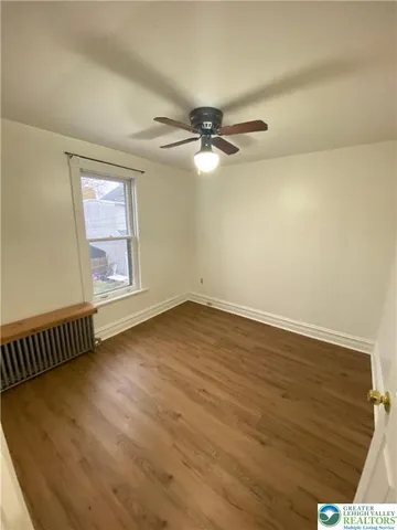 an empty room with wooden floor fan and windows