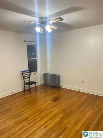 a view of an empty room with wooden floor and a ceiling fan