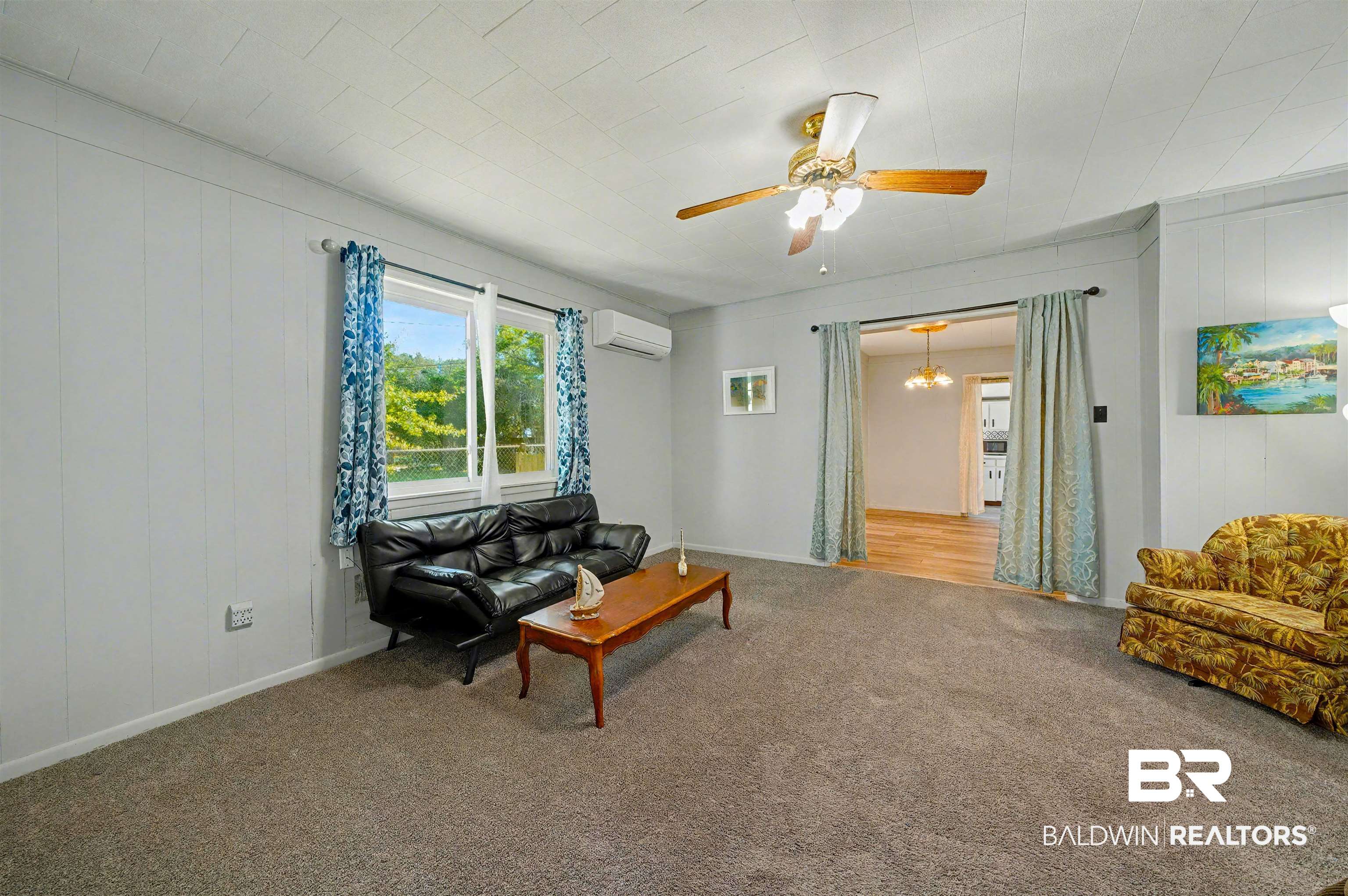 209 West Magnolia Avenue Foley, AL 36535 - Photo 9 of 23 Carpeted living room with wooden walls, a ceiling fan, an AC wall unit, and a chandelier