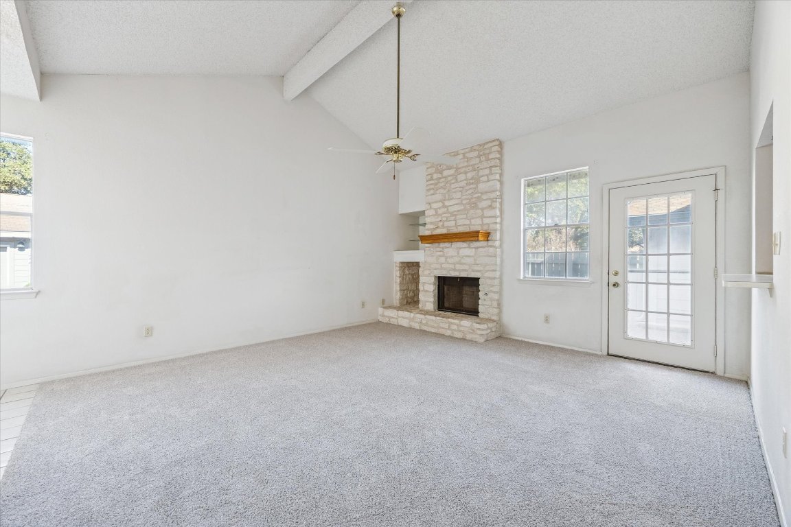 6501 Brush Country Road, Unit 120 Austin, TX 78749 - Photo 11 of 35 Unfurnished living room featuring beam ceiling, a fireplace, a textured ceiling, carpet floors, and ceiling fan