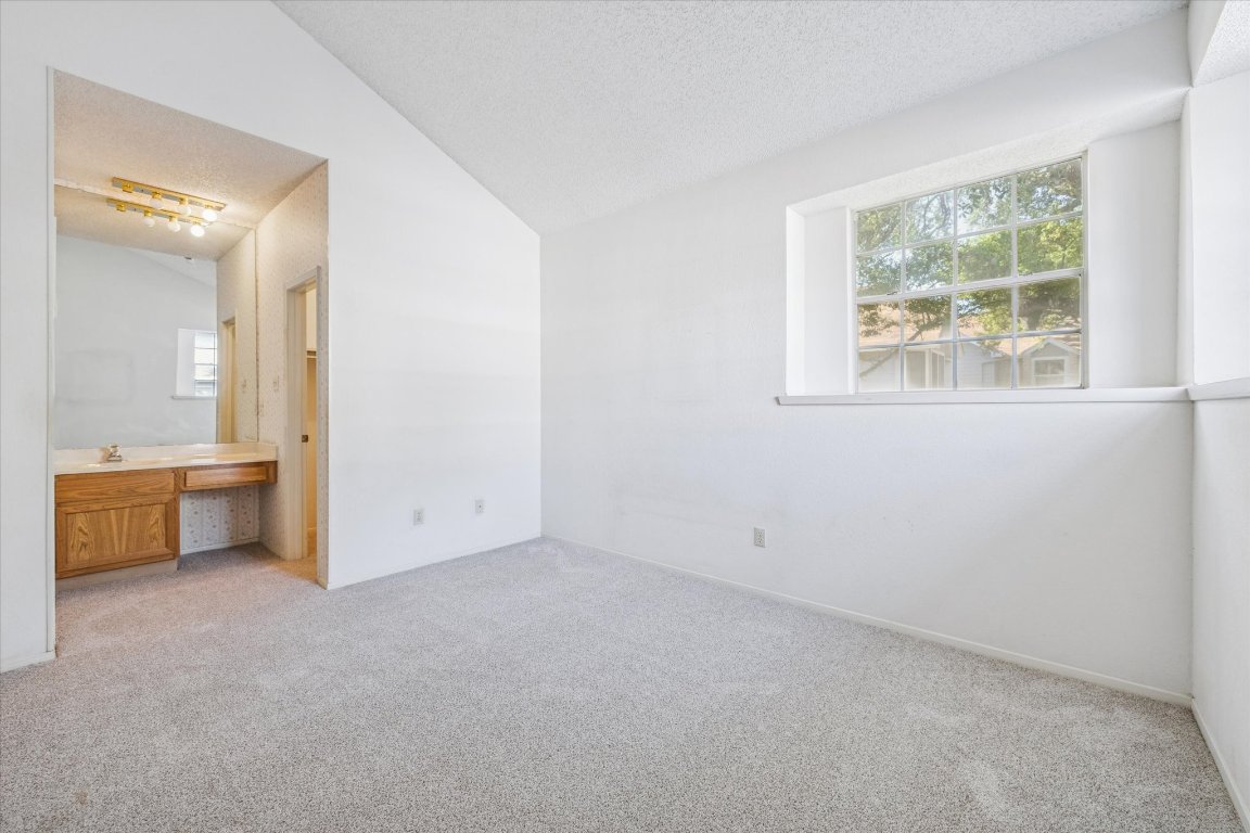 6501 Brush Country Road, Unit 120 Austin, TX 78749 - Photo 12 of 35 Unfurnished bedroom featuring lofted ceiling, light carpet, built in desk, multiple windows, and a textured ceiling