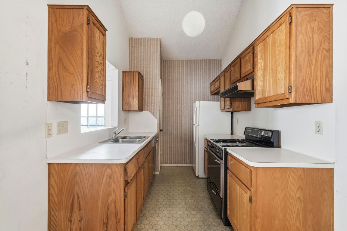 6501 Brush Country Road, Unit 120 Austin, TX 78749 - Photo 13 of 35 Kitchen featuring black gas range oven, light countertops, under cabinet range hood, brown cabinetry, and hanging light fixtures