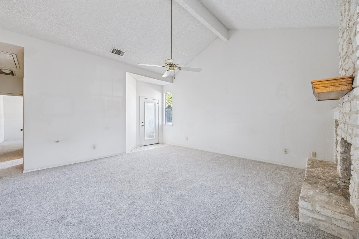 6501 Brush Country Road, Unit 120 Austin, TX 78749 - Photo 10 of 35 Unfurnished living room featuring carpet flooring, a textured ceiling, beamed ceiling, ceiling fan, and a fireplace