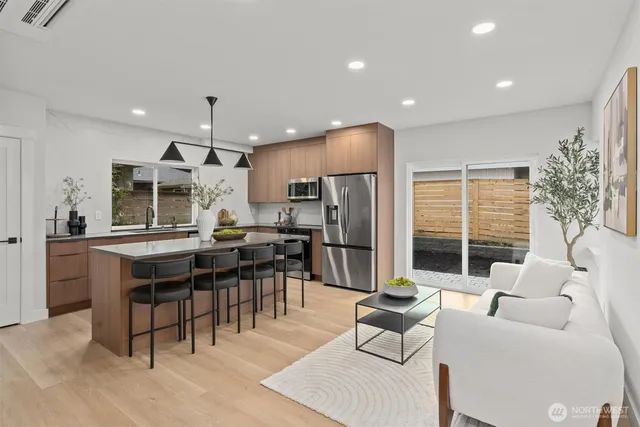 a open kitchen with stainless steel appliances kitchen island granite countertop a refrigerator a stove a dining table and chairs with wooden floor