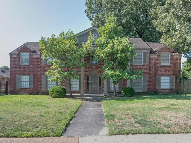 a front view of brick house with yard and trees