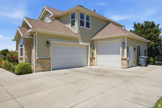 1263 East 1200th South Springville, UT 84663 - Photo 53 of 60 Exterior featuring light green siding, stone accents, two white garage doors, a concrete driveway, and mature landscaping