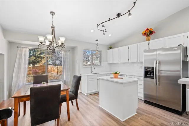 a kitchen with stainless steel appliances granite countertop a refrigerator a sink dishwasher a dining table and chairs with wooden floor