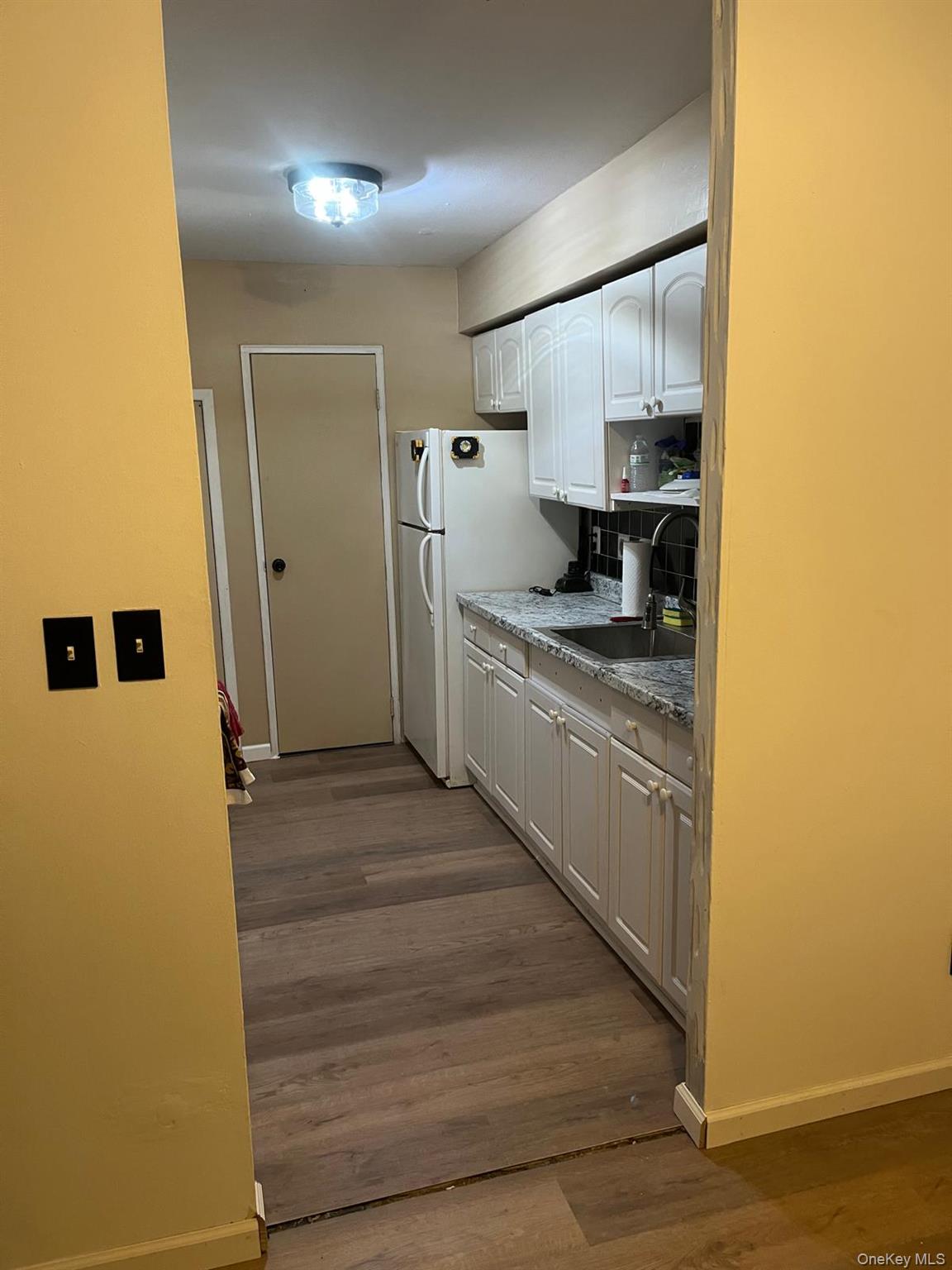 2 Williamsburg Court, Unit C Ridge, NY 11961 - Photo 9 of 20 Kitchen with white cabinetry, freestanding refrigerator, backsplash, wood-type flooring
