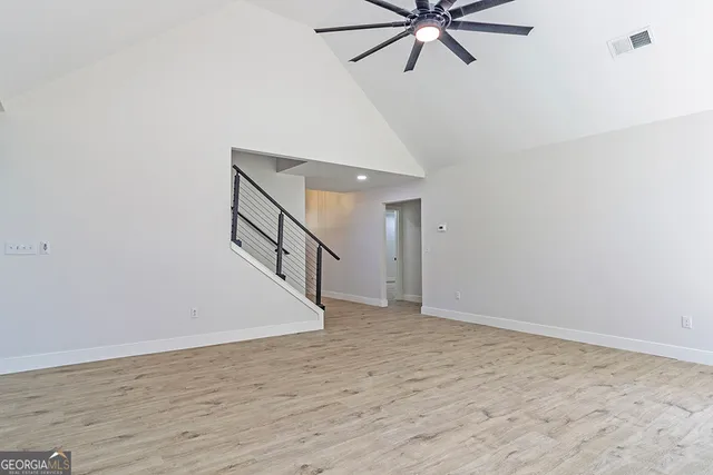 a view of an empty room with wooden floor and a ceiling fan