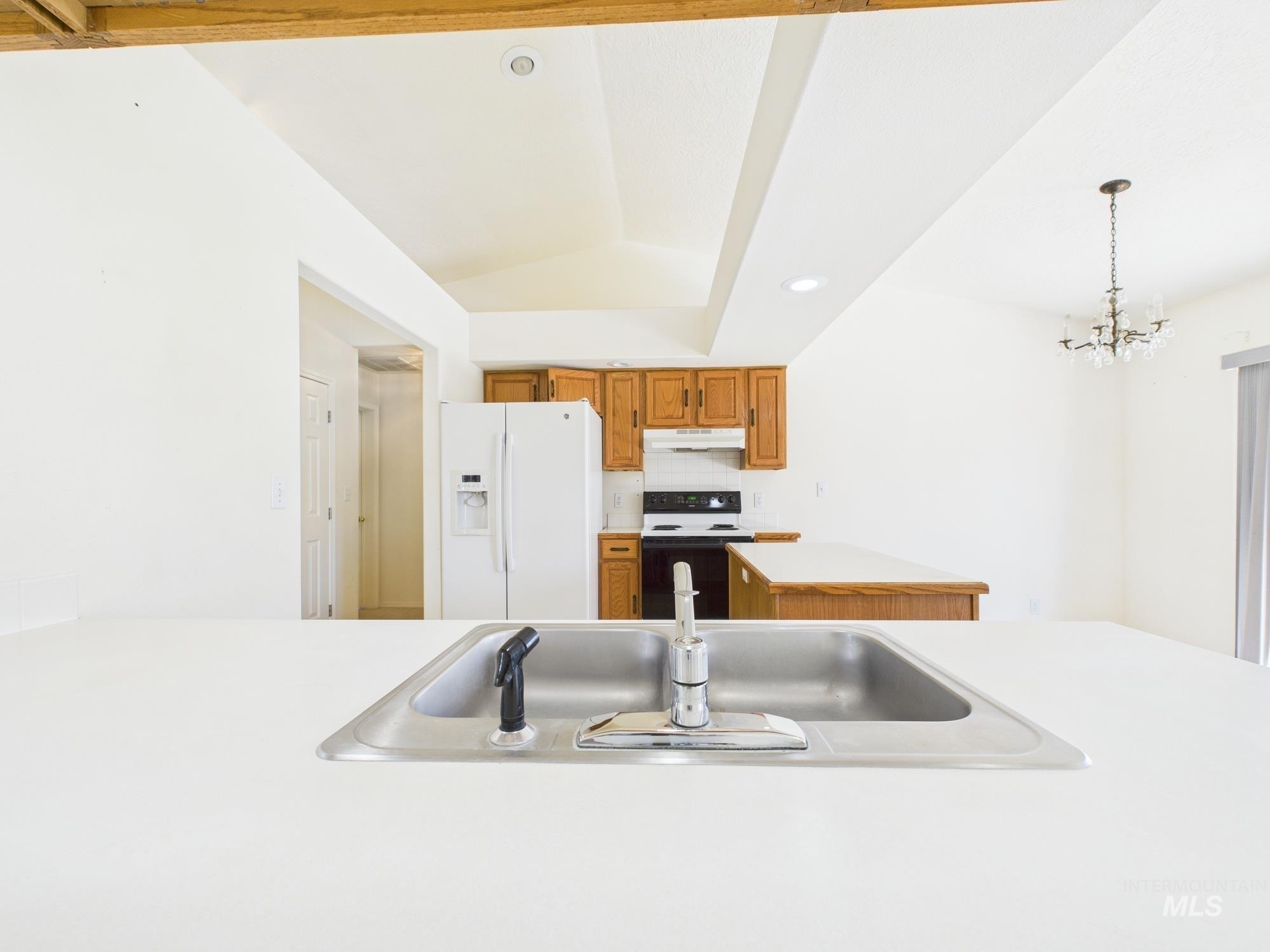1786 North Plaza Road Emmett, ID 83617 - Photo 6 of 36 Kitchen with brown cabinetry, light countertops, white refrigerator with ice dispenser, range with electric cooktop, and hanging light fixtures
