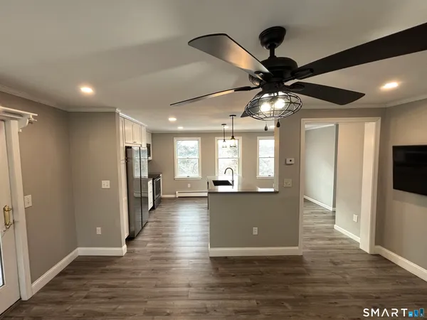 a view of an empty room and kitchen view with wooden floor