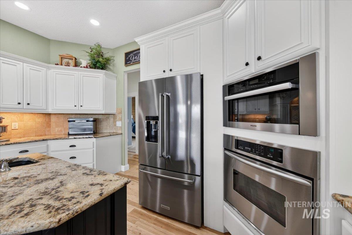 414 East Shafer View Drive Meridian, ID 83642 - Photo 12 of 50 Kitchen featuring white cabinetry, stainless steel appliances including a KitchenAid French Door Refrigerator w/water & Ice & Bottom Freezer, a KitchenAid built-in oven and a Miele microwave, natural hickory hardwood flooring, and granite countertops